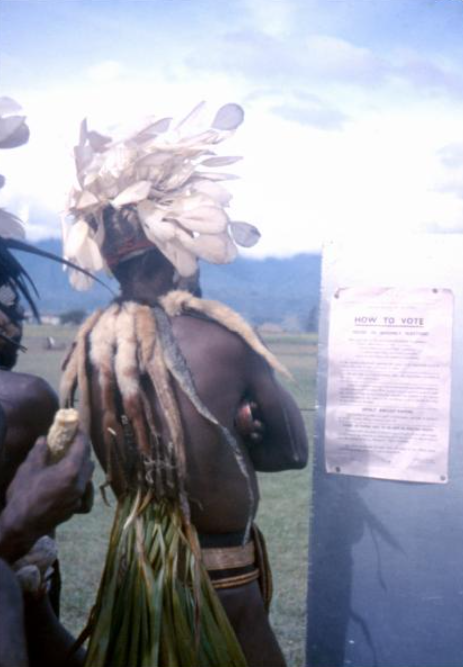 Man in traditional dress with feather headdress reading election sign