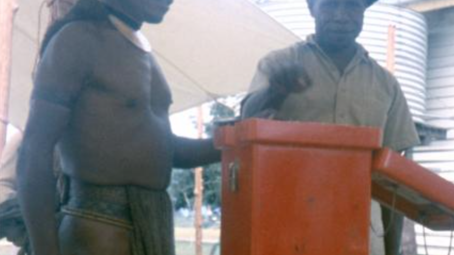 Man in ceremonial dress with feather headdress voting.