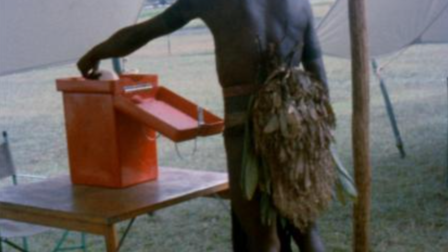 Man in ceremonial dress with feather headdress voting